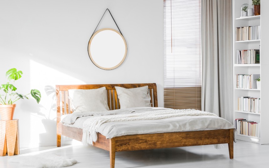 A bed with a rustic wooden bed frame in a natural, sunlit bedroom interior with white walls